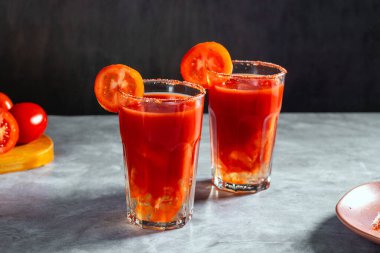 İki sebze, koyu gri arka planda cam içinde sallanmış kokteyller. Kırmızı domates kokteyli. Domates dilimiyle servis edilmiş. Vegan menüsü.