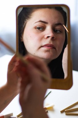 Millennial Kafkas kadınının dikey görüntüsü aynaya bakarak kaşlarını boyuyor. Aynadaki yansıma. Hazırlanıyor. Güzellik konsepti.