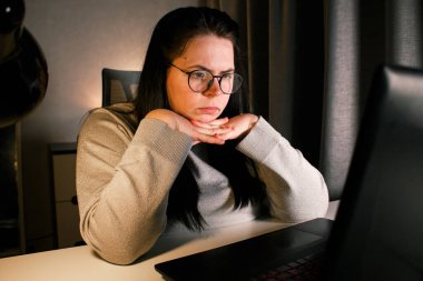 Akşam geç saatlerde dizüstü bilgisayarda çalışan bir kadın. Yoğunlaştırılmış kadın çalışan, çalışma masasındaki bilgisayarda oturan iş sorunlarını çözer