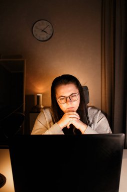 Akşam geç saatlerde dizüstü bilgisayarda çalışan bir kadın. Yoğunlaştırılmış kadın çalışan, çalışma masasındaki bilgisayarda oturan iş sorunlarını çözer