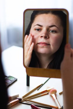 Millennial Kafkas kadınının aynaya bakarken makyaj yaparken yüz kremi sürüşünün dikey görüntüsü. Aynadaki yansıma. Hazırlanıyor. Güzellik konsepti.