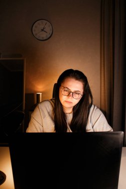 Akşam geç saatlerde dizüstü bilgisayarda çalışan bir kadın. Yoğunlaştırılmış kadın çalışan, çalışma masasındaki bilgisayarda oturan iş sorunlarını çözer