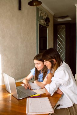 Ev mutfağında dizüstü bilgisayar kullanan küçük kızı olan mutlu bir anne. Okul projesi üzerinde çalışıyorum. Teknolojileri kullanarak ev ödevlerine yardım etmek