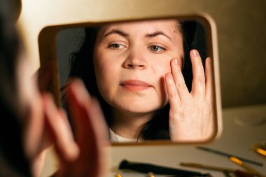 Makyajdan önce yüzüne nemlendirici krem süren ve aynaya bakan bir kadın. Deri bakımı konsepti. Kendi kendine makyaj. Cilt bakımı. Aynadaki yansıma