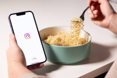Evde makarna yerken akıllı telefonda Instagram uygulaması kullanan bir kadın. Ekranda Instagram logosu var. Sosyal medya kavramı ile yemek yemek