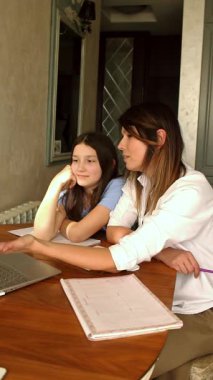 Ev mutfağında dizüstü bilgisayar kullanan küçük kızı olan mutlu bir anne. Okul projesi üzerinde çalışıyorum. Teknolojileri kullanarak ev ödevlerine yardım etmek