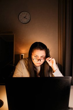 Gözlüklü genç bir kadın gece geç saatlerde evde bilgisayar başında çalışıyor, modern teknolojileri kullanıyor ve çevrimiçi eğitim alıyor. Uzaktan öğrenme konsepti. Online üniversite. Sürece odaklan.