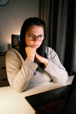 Akşam geç saatlerde dizüstü bilgisayarda çalışan bir kadın. Yoğunlaştırılmış kadın çalışan, çalışma masasındaki bilgisayarda oturan iş sorunlarını çözer