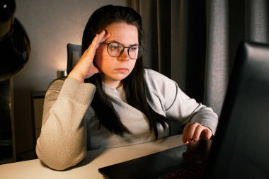 Akşam geç saatlerde dizüstü bilgisayarda çalışan bir kadın. Yoğunlaştırılmış kadın çalışan, çalışma masasındaki bilgisayarda oturan iş sorunlarını çözer