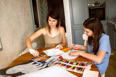 Anne ve kızı birlikte resim yaparken gülüyorlar, şefkatli anlarını paylaşıyorlar. Kaygısız çocukluk ve nitelikli ebeveyn ilişkisinin dokunaklı sahnesi