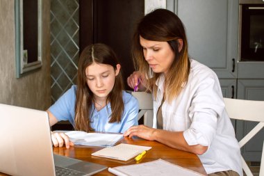 Anne ve kızı internette dizüstü bilgisayarda sörf yapıyor mutfakta oturuyor, online alışveriş yapıyor. İnternette heyecan verici bir şey izliyorum.