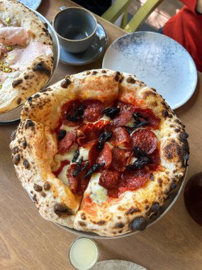 Geleneksel pizza fırında pişirilir ve restoranda eritilmiş peynir, et ve şam fıstığı ile servis edilir. Alternatif tat