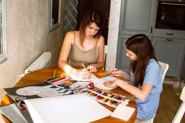 Anne ve çocuk mutfak masasında çizim yaparken eğleniyorlar. Sıcak aile sahnesi, oyun oynayarak öğrenme ve birliktelik. Annelik, yaratıcılık ve aile mutluluğu temaları için ideal