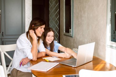 Kızı, internette dizüstü bilgisayarda heyecanlı bir şey gösteriyor. Mutfakta masada oturuyor. Ebeveynliğin ve anneliğin kutlu olsun. Mutlu aile kavramı