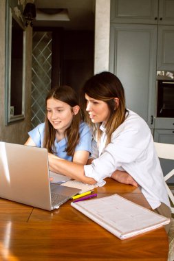 Anne ve kızı evde otururken dizüstü bilgisayar kullanıyorlar. Anne okul ödevlerinde çocuğa yardım ediyor. Modern teknolojilerle eğitim