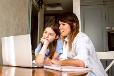 Anne ve kızı evde otururken dizüstü bilgisayar kullanıyorlar. Anne okul ödevlerinde çocuğa yardım ediyor. Modern teknolojilerle eğitim