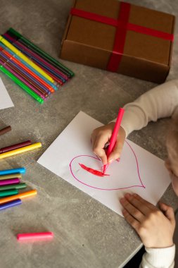 Küçük ellerin kalem tutması çocukça sanat eserleri yaratıyor. Çocuk kırmızı kalp çizmek ve yaratmak için zaman harcıyor.