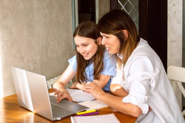 Aile dijital eğlence zamanı. Kafkas anne ve kızı dizüstü bilgisayar kullanarak online aktiviteler yapıyor, internette sörf yapıyor, iç mekanlarda video görüşmeleri yapıyor.