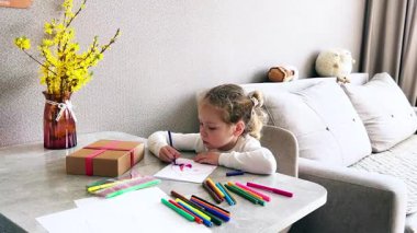 Küçük kız oturma odasındaki masada otururken çizim işlemine daldı. Çocuk eğitimi, ebeveynlik ve çocuk gelişimi kavramları için mükemmel