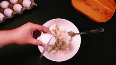 Syrniki yapma süreci. Birinci adım: süzme peynire yumurta eklemek. Siyah yüzeyin en üst görüntüsü. Rus mutfağı.