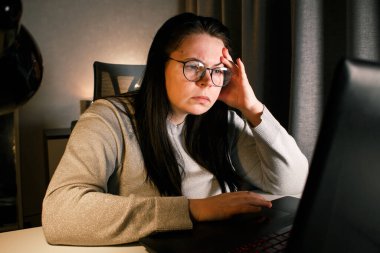 Gözlüklü genç bir kadın gece geç saatlerde evde bilgisayar başında çalışıyor, modern teknolojileri kullanıyor ve çevrimiçi eğitim alıyor. Uzaktan öğrenme konsepti. Online üniversite. Sürece odaklan