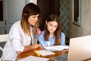 Ev mutfağında dizüstü bilgisayar kullanan küçük kızı olan mutlu bir anne. Okul projesi üzerinde çalışıyorum. Teknolojileri kullanarak ev ödevlerine yardım etmek