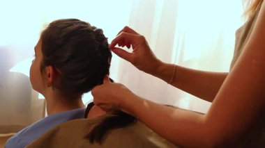 Annenin, kızının saçına örgü ören ellerine yakın çekim. Okuldan önce güzel kızlar ve kadınsı bağlar. Otantik ebeveynlik anı