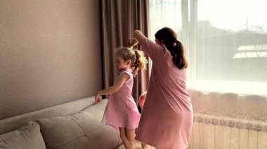 Dört yaşındaki bir kız ve annesi pembe elbiseler içinde birlikte dönüp gülüyorlar. Anne kızının eğlencesinin ve bağlantısının yürek ısıtan gösterisi.
