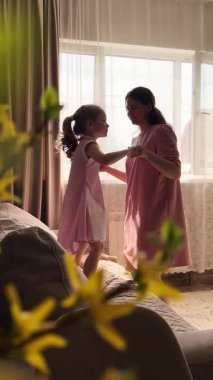 Tasasız çocukluk anı. Anaokulu kızı ve annesi evde pembe elbiseler içinde dans ediyorlar. Ebeveynlik ve mutluluk temaları için ideal