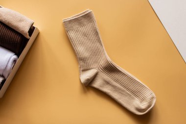 Canlı sarı yüzeye yerleştirilmiş bej çorap çifti, yakınlarda katlanmış çorapların toplanması, kumaş dokusu ve renk çeşitliliği şık bir düzende vurgulanıyor