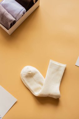 Bej yüzeyde tırtıklı beyaz çoraplar, yakınlarda renkli katlanmış çoraplar, şık tekstil tercihleri ve rahat moda. Dikey düzlük.