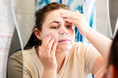 Yüz temizleyici kullanan bir kadın. Organik güzellik ya da temiz cilt pazarlaması için özgün bir an. Aynadaki yansıma. Uluslararası kişisel bakım günü