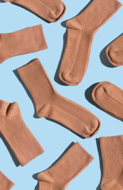 Açık mavi yüzeyde bej çorapların düzenlenmesi, farklı dokuları ve stilleri vurgulamak, moda, tekstil tasarımı ve yaratıcı projeler için mükemmel. Dikey.