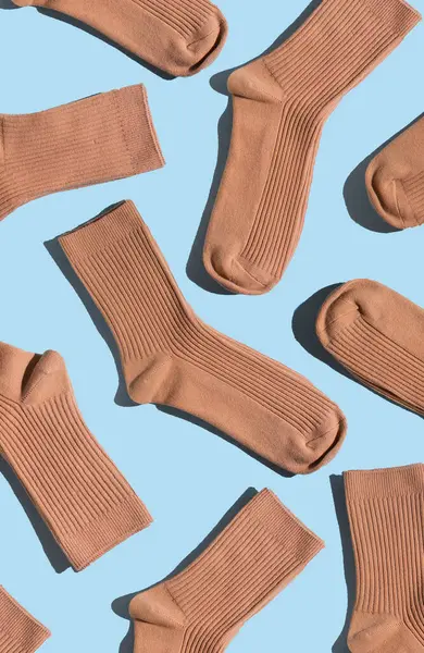 Açık mavi yüzeyde bej çorapların düzenlenmesi, farklı dokuları ve stilleri vurgulamak, moda, tekstil tasarımı ve yaratıcı projeler için mükemmel. Dikey.