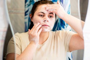 Kadın makyajı yüz temizleme köpüğüyle temizliyor. Banyo aynasında yansıma. Güzellik rutini. Dermatoloji kavramı