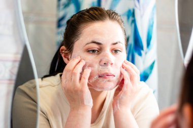 Kadın köpüklü yıkamayla yüz temizleme ayini yapıyor. Sağlık ve cilt bakımı ürünleri. Uluslararası Kişisel Bakım Günü