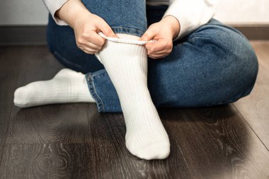 Ahşap zeminde oturan ve beyaz çorap giyen kot giyen bir kadın. Günlük rutin temalar.