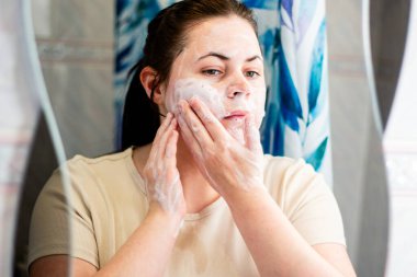 Kadın köpüklü yıkamayla yüz temizleme ayini yapıyor. Sağlık ve cilt bakımı ürünleri. Uluslararası Kişisel Bakım Günü