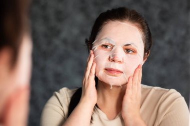 Kadın banyoda nemlendirici yüz maskesi takıyor. Güzellik rutini. Uluslararası Kişisel Bakım Günü