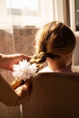 Anne ellerinin kızının güzel saçlarına narin bir örgü ördüğü yakın plan. Kadınsı bir bağ ve özen anı.