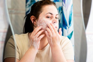Sabah cildi rutini. Kadın yüzünü banyoda köpükle temizliyor. Uluslararası kişisel bakım günü
