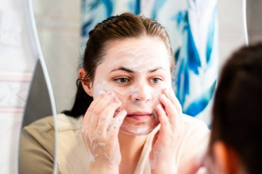 Sabah cildi rutini. Kadın yüzünü banyoda köpükle temizliyor. Uluslararası kişisel bakım günü