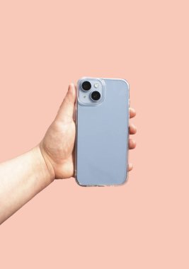 Elinde şeffaf telefon kılıfı var. Pastel arka planda temiz bir tasarım sergiliyor. Ürün özelliklerini ve faydalarını göstermek için ideal