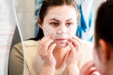 Kadın makyajı yüz temizleme köpüğüyle temizliyor. Banyo aynasında yansıma. Güzellik rutini. Dermatoloji kavramı