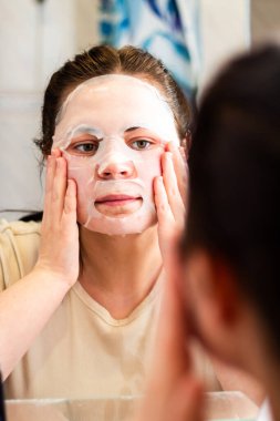 Geç saatte cilt bakımı rutini. Nemlendirici yüz maskesi takan bir kadın. Banyo aynasında yansıma. Dermatoloji kavramı