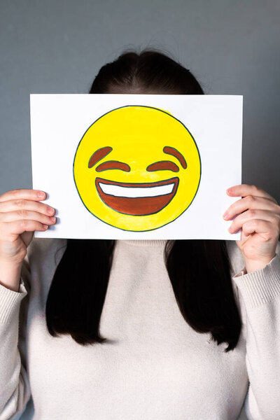 Женщина в счастливой улыбающейся маске смайлика перед лицом. Тенденции социальных медиа, Gen Z маркетинг, Всемирный день смайликов 17 июля.