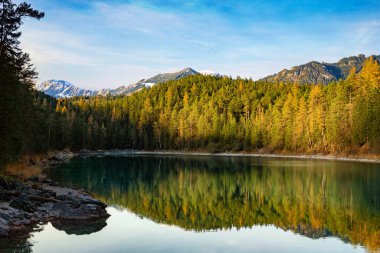 Eibsee Gölü 'ndeki Alman Alp Dağları manzarası ve ormanın arkasındaki tepeleri gösteren bir göl.