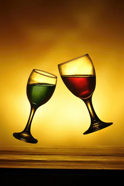 two wine glasses filled with green and red water were tossing each other in the air