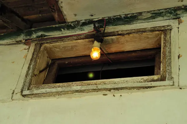a light bulb that was on and installed in the middle of a house window that was in a damaged condition