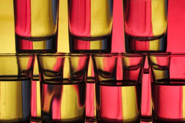 İki renkli arkaplanda katmanlı su dolu küçük bardak koleksiyonu ışık kırılmasına neden olur.